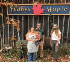 Four members of the Yeany family stand in front of the sign for Yeany's Maple.